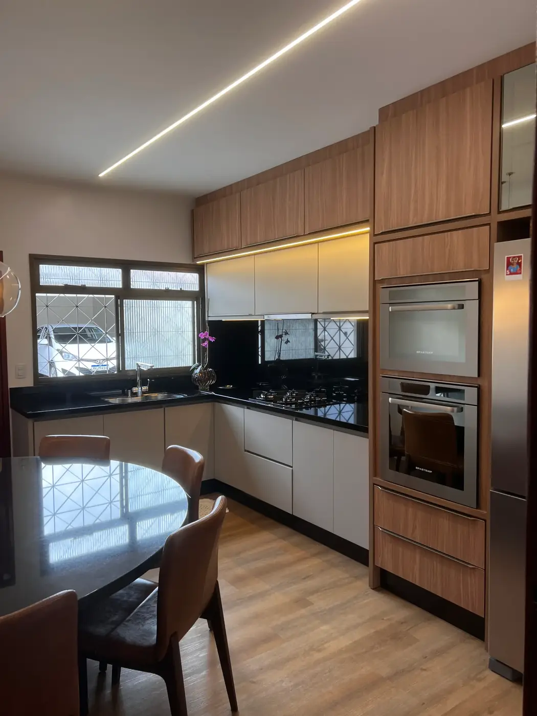 Cozinha amadeirada com bancada preta e torre de fornos